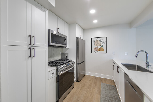 Renovated Package I kitchen with stainless steel appliances, white quartz countertops, white cabinetry, light grey tile backsplash, and hard surface flooring - Avalon Woodland Hills Apartments