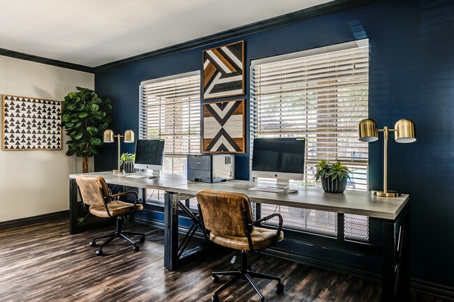 The business center of an apartment community is shown with two Apple desktop computers, leather chairs, and modern lighting.