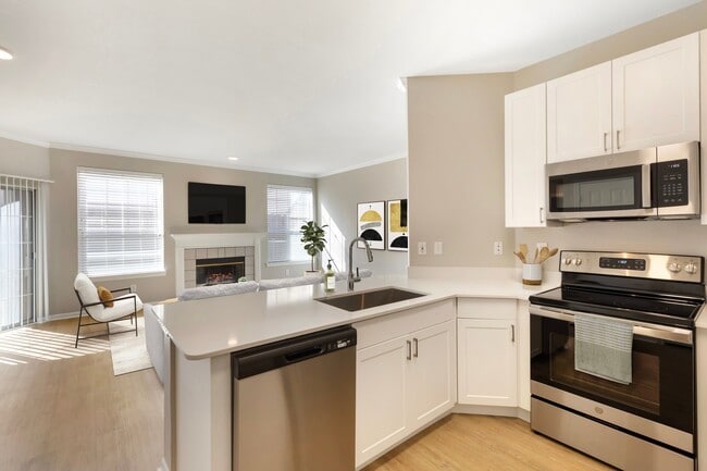 Renovated Package I kitchen with stainless steel appliances, white speckled quartz countertop, white cabinetry, and hard surface flooring - Avalon Addison Apartments