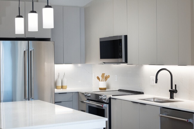Signature Collection kitchen with stainless steel appliances, light grey cabinetry, marbled quartz countertops and backsplash, under-cabinet lighting, and pendant lighting - Avalon at Becker Farm