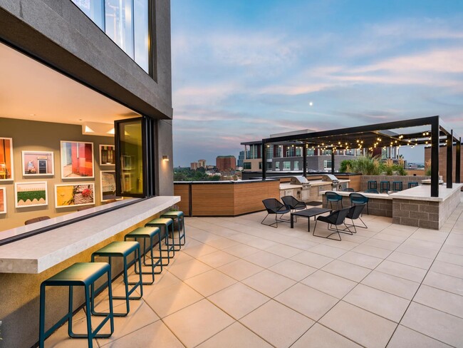 Rooftop lounge with bar seating, grill stations, and shaded spaces for casual hangs or evening gatherings under the string lights.