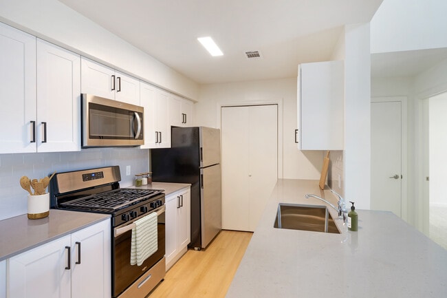 New Apartments kitchen with new stainless steel appliances, grey quartz countertops, grey subway tile backsplash, and hard surface flooring - Avalon Commons Apartments