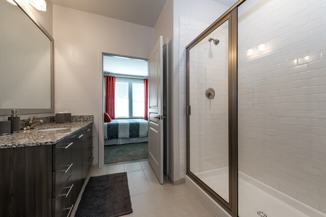Bath with granite countertops, brown cabinetry, hard surface flooring and tiled shower