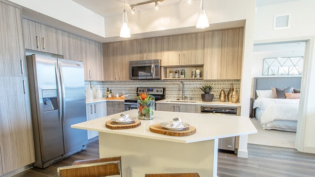 Open-concept luxury apartment kitchen with quartz island, stainless steel appliances, and wood cabinetry - Griffis North Olive