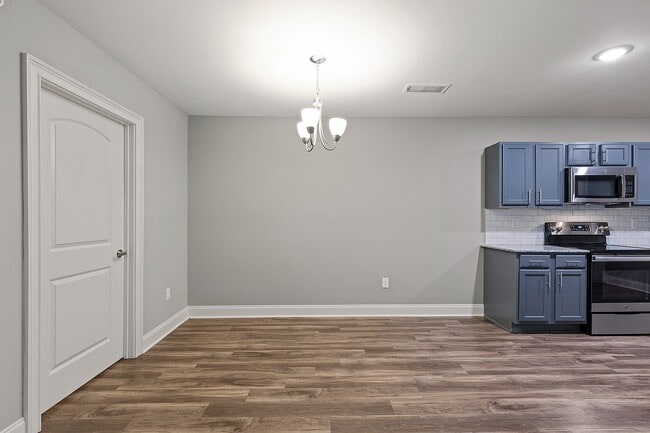 Modern kitchen & dining space with sleek gray cabinetry and stainless steel appliances, complemented by elegant wood flooring and a stylish overhead chandelier.