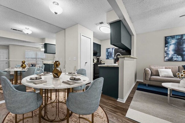 Open-plan dining area with marble round table, blue chairs, gold accents, kitchen beyond, and living room with sofa