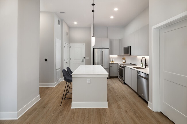 Signature Collection kitchen with stainless steel appliances, light grey cabinetry, marbled quartz countertops and backsplash, under-cabinet lighting, and hard-surface flooring - Avalon at Becker Farm