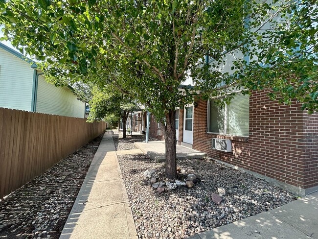 Un encantador sendero bordeado de frondosos árboles verdes conduce a un edificio de apartamentos de ladrillo, ofreciendo un ambiente residencial sereno y acogedor. - 10756 West 12th Lane